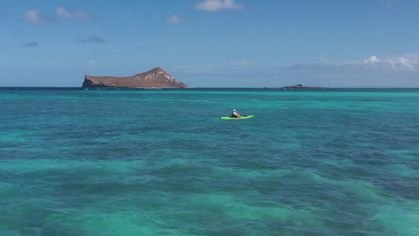 Person paddles kayak in ocean between island and shore