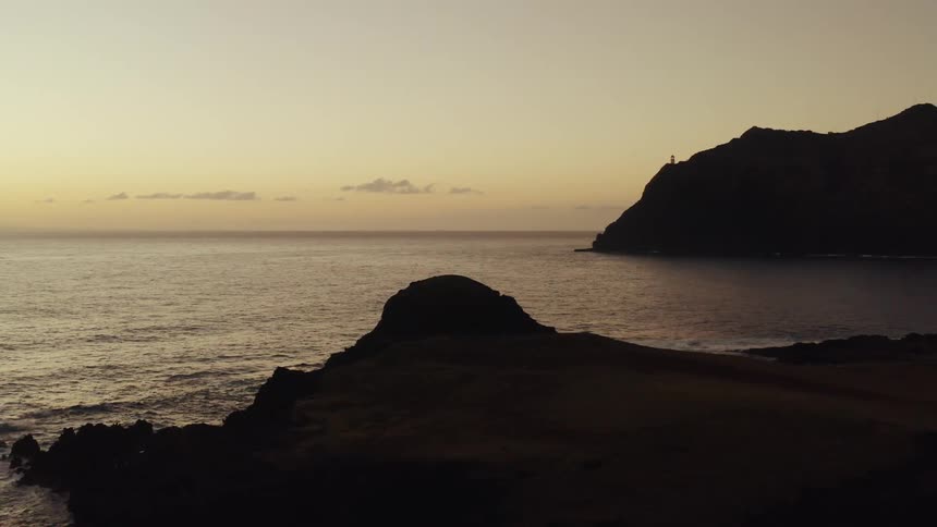 Rocky coastline at sunset with lighthouse in distance