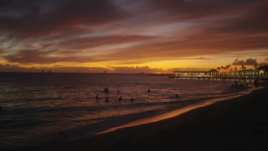 Office buildings overlook beach with swimmers at sunset