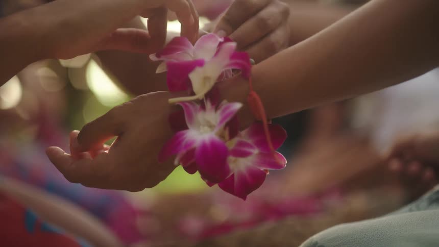 Woman ties bracelet made of flowers onto another persons wrist