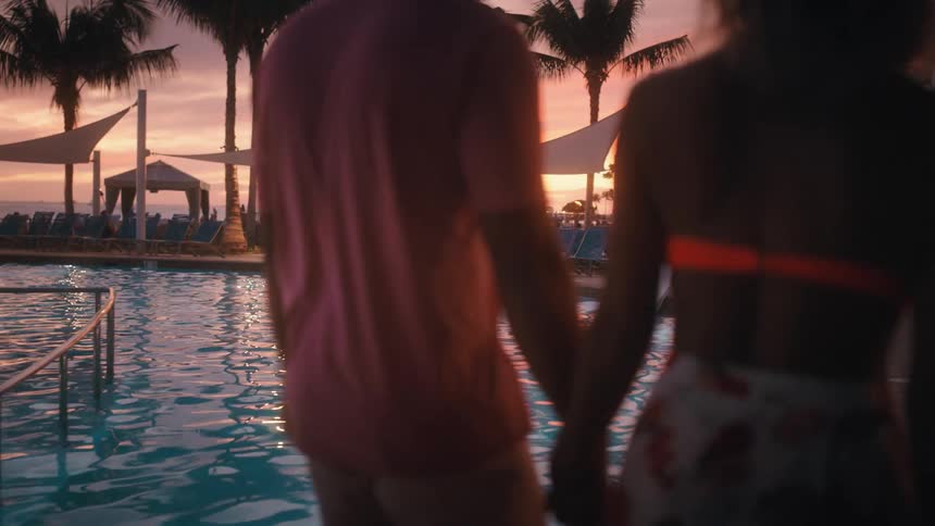 Romantic couple taking sunset walk by the pool at a resort