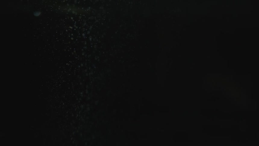 Raindrops slowly falling with lights reflecting off of it