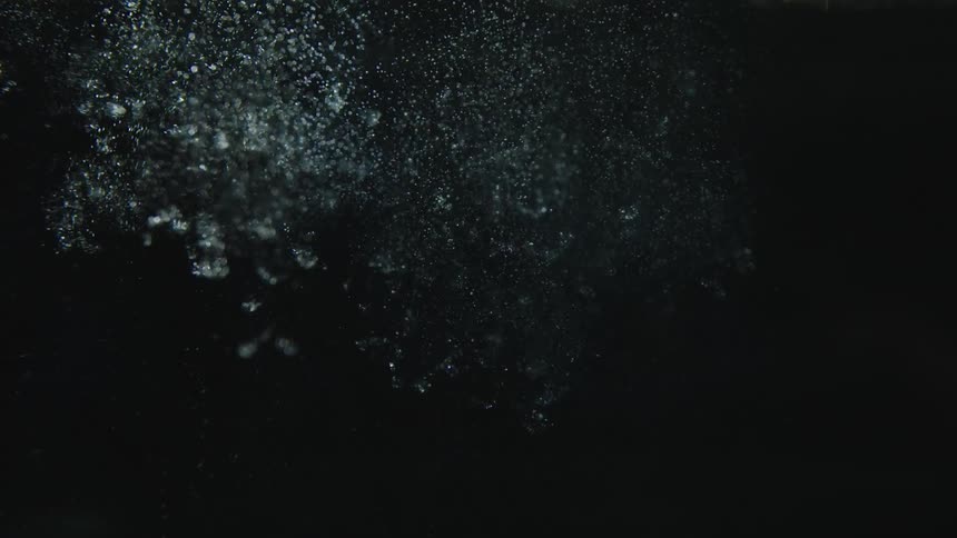 Small pieces of glass sinking on water leaving air bubbles trails