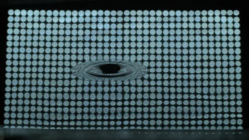 A water drop dropping into water that is reflecting blue circles in a grid