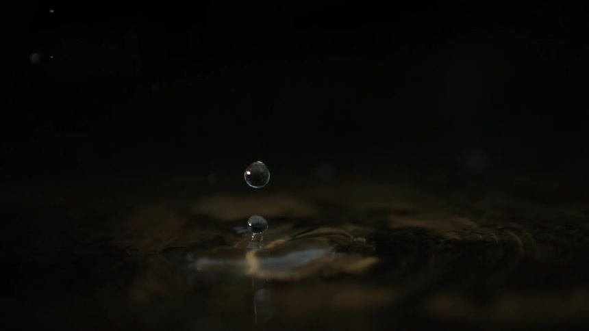 Water drops fall on a water surface on a dark background