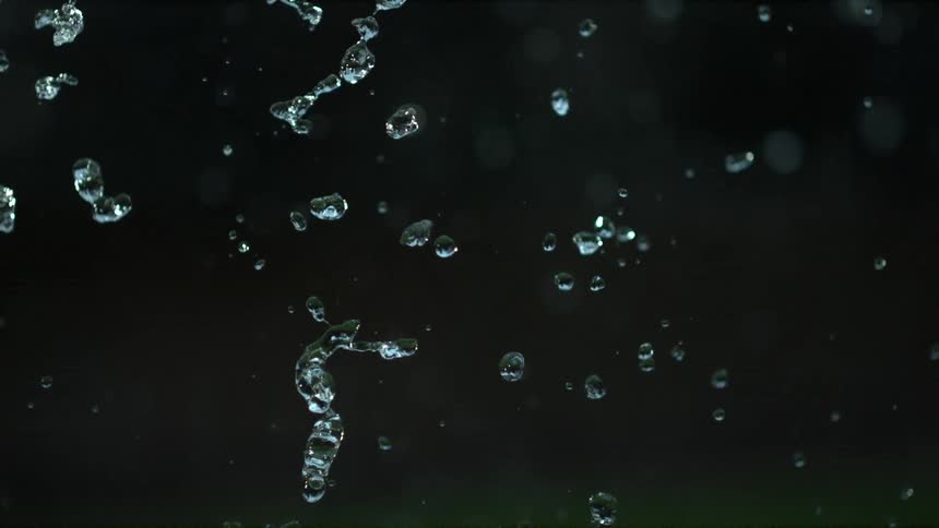 Drops of water fall in slow motion in front of a black background