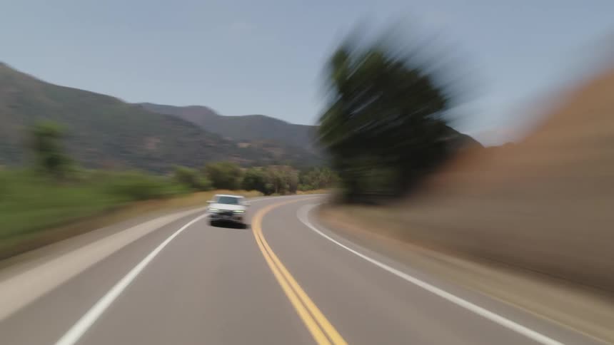 A car speeds along a curvy road next to a mountain range