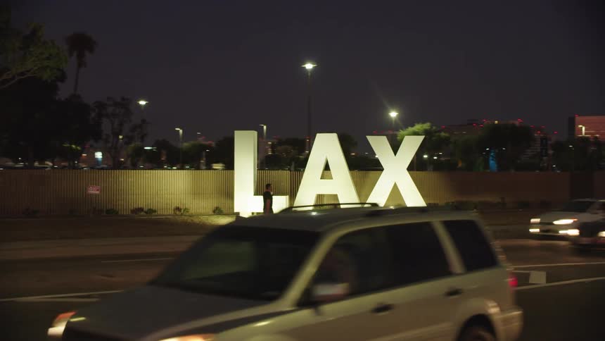 Man walking by lax airport sign at night while cars drive by