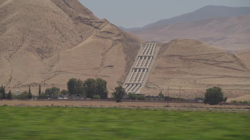 Traveling past green crop fields with large pipes coming down the slope of a hill