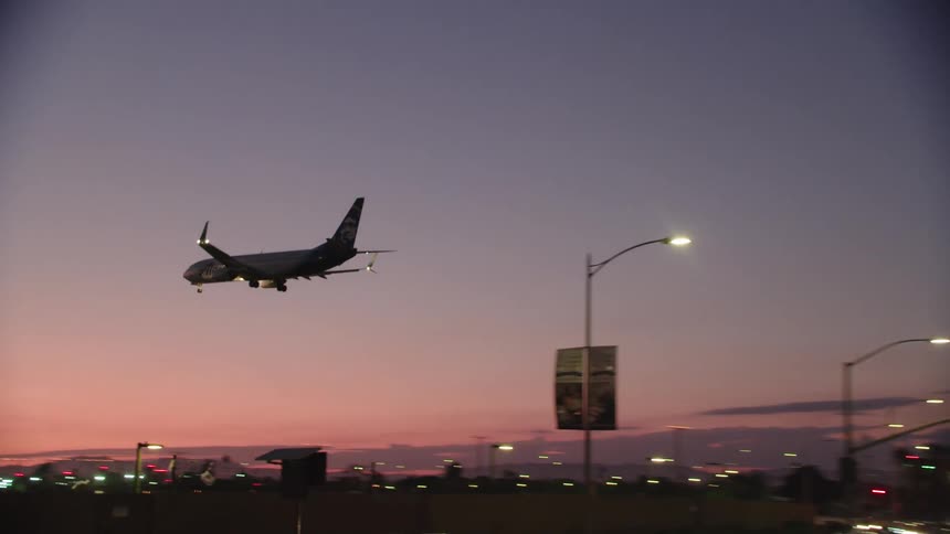 An airplane flies over a highway as it heads towards a runway to land
