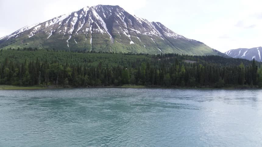 Aerial view of a snow covered mountain surrounded by pine forest in front of lake