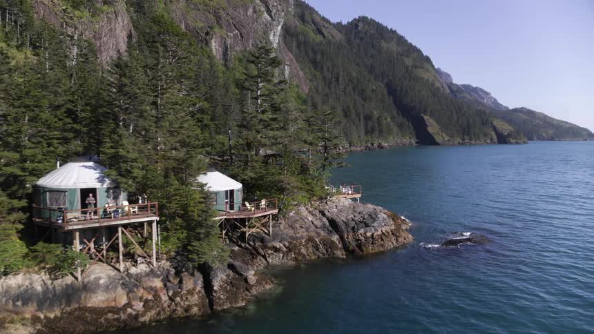A man walks out of a building on to a deck and looks out over the water