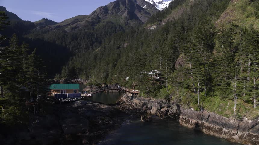 Two people walk across a bridge towards a house