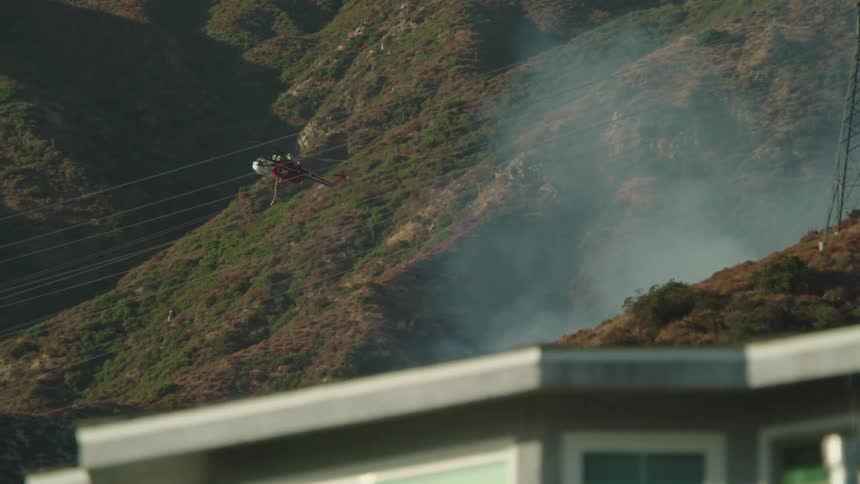 Helicopter flies over smoke from wildfire behind neighborhood