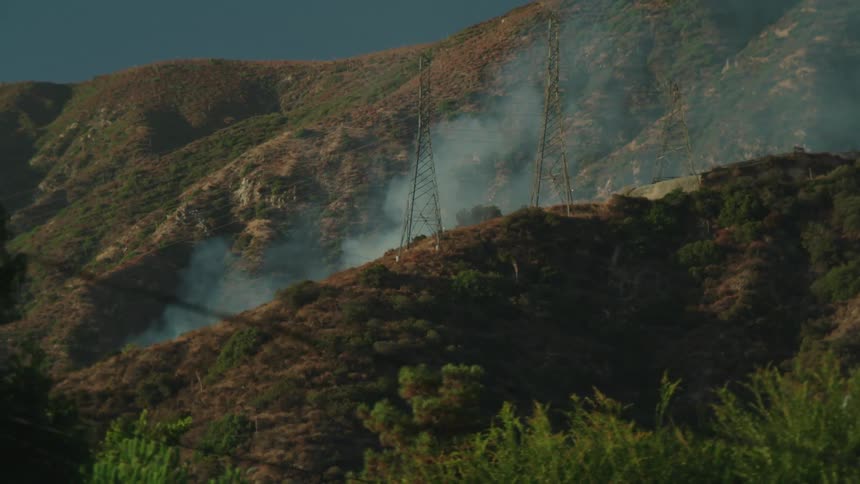 Smoke rises from the slope of a hill near a neighborhood