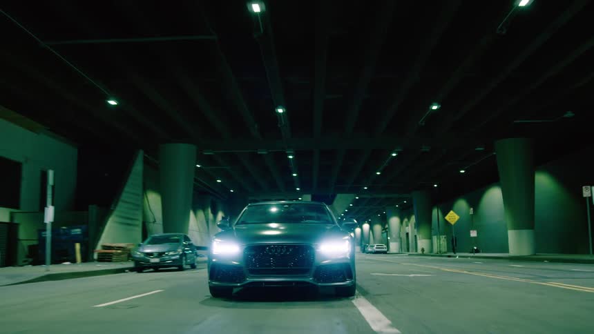 Car driving through underpass between buildings at night