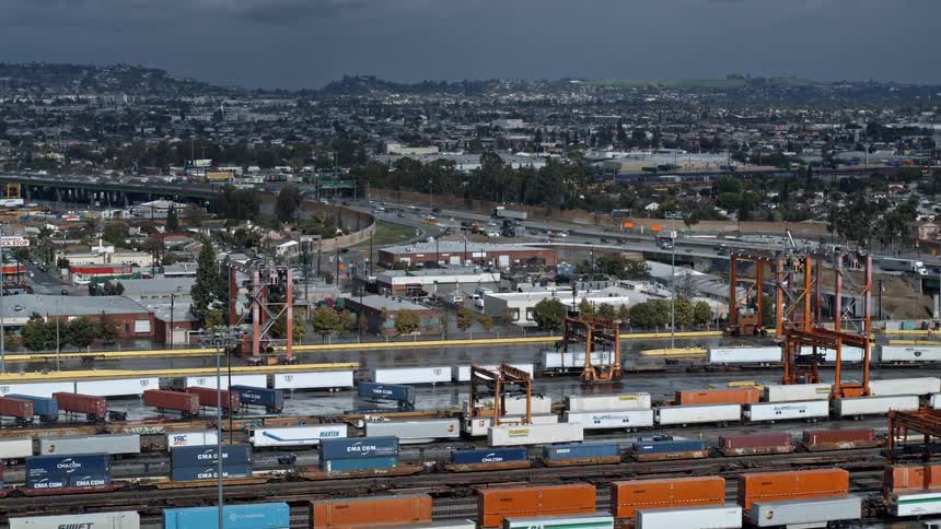 Shipping vehicles sit in a lot with traffic moving in the background