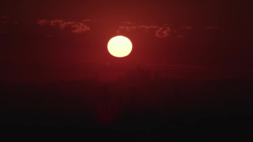The full moon glows in a reddish sky with silhouettes of trees and branches