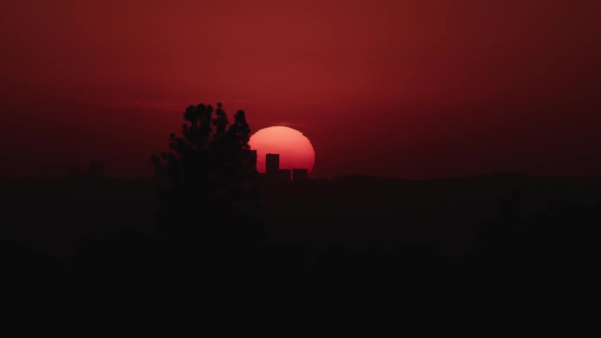 Sun sets in dark red sky behind silhouette of city skyline
