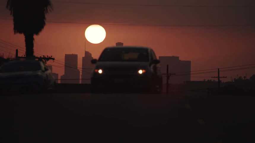 Sun sets in red sky behind silhouette of city skyline