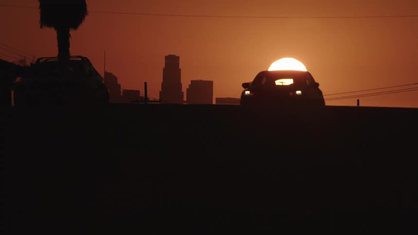 Two cars drive down a street out of a city at sunset