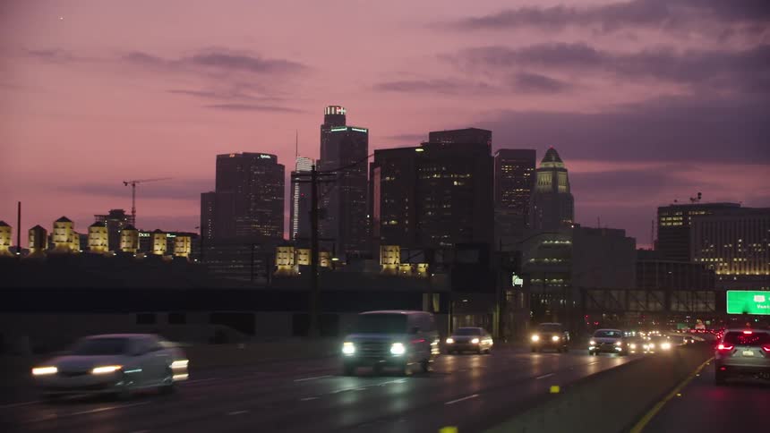 City skyline with tall buildings and cars driving on the highway at dusk