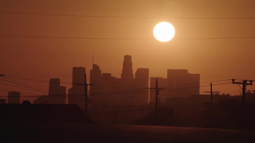 A perfectly round glowing sun in a red sky over a city skyline