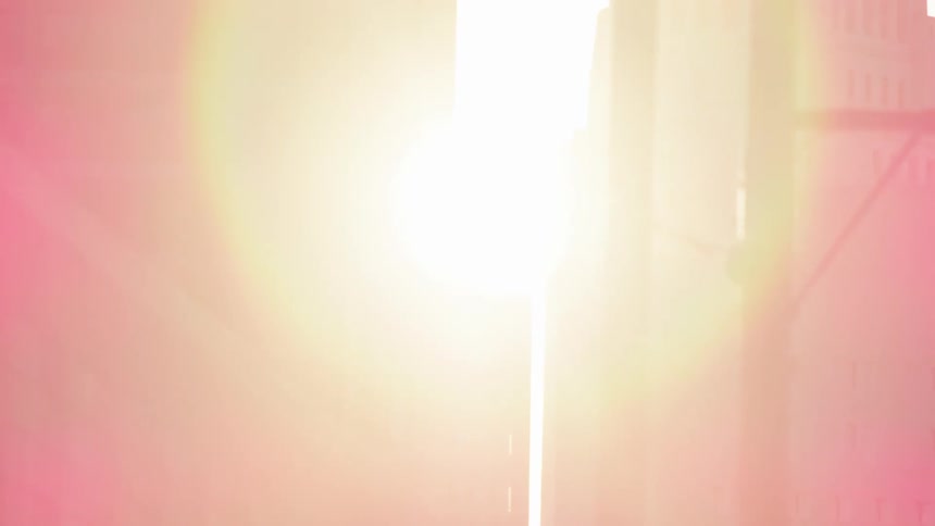 Sun shines through the space between two large buildings in a city
