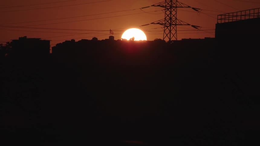 Sun sets in dark orange sky behind silhouettes of city buildings