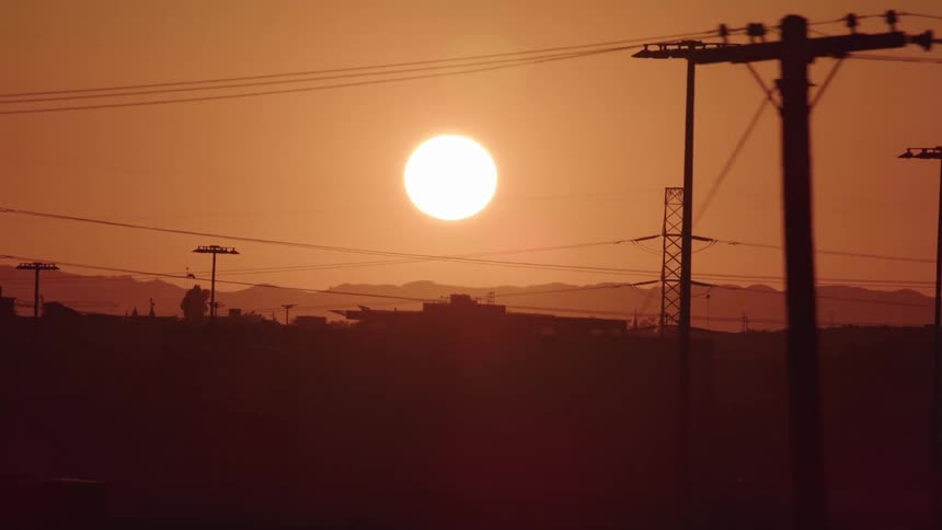 Sun sets over the mountains in front of power lines