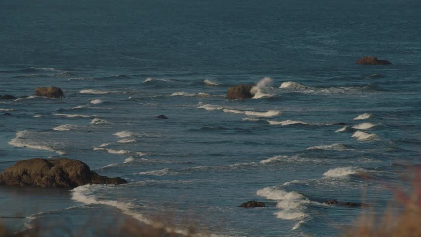 Foam tipped waves rush through large boulders towards the shore