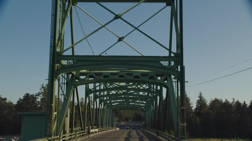 Vehicles drive down a two lane bridge near a forest