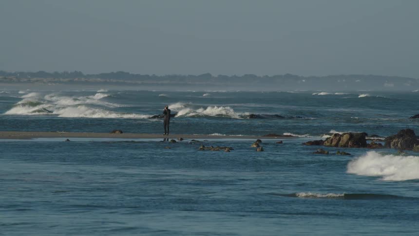 A man stands on the shore and looks out at the water