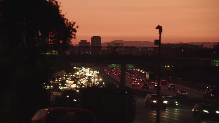 Headlights and tail lights glow as traffic fills a city highway at sunset