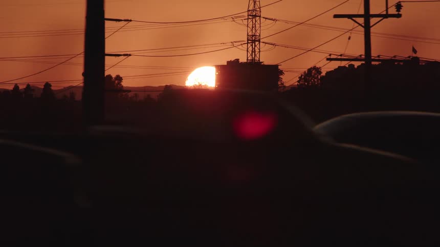 Sun sets in dark orange sky behind silhouette of town and traffic