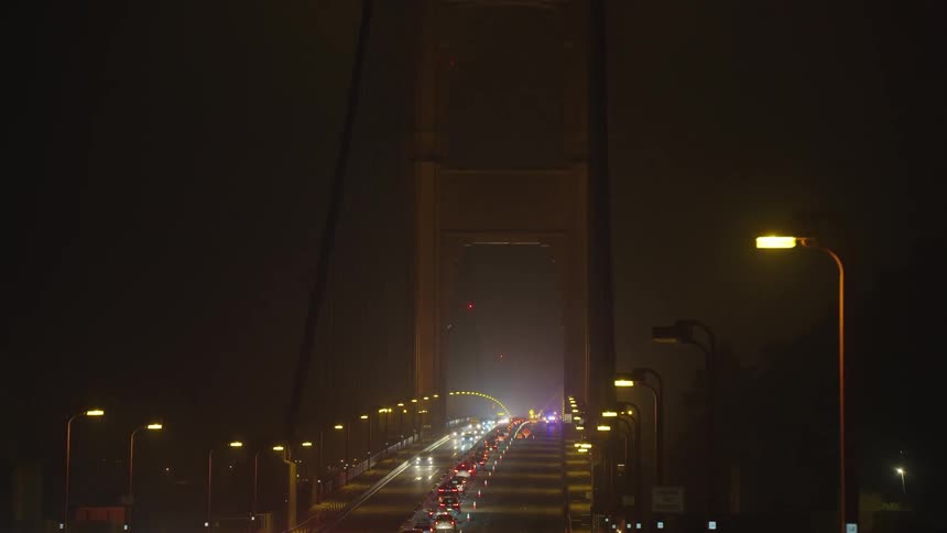 Thick traffic over a large bridge on a foggy night