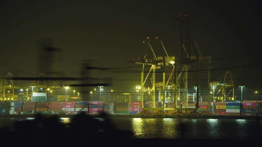 Cargo containers are stacked high in a ship yard along the water