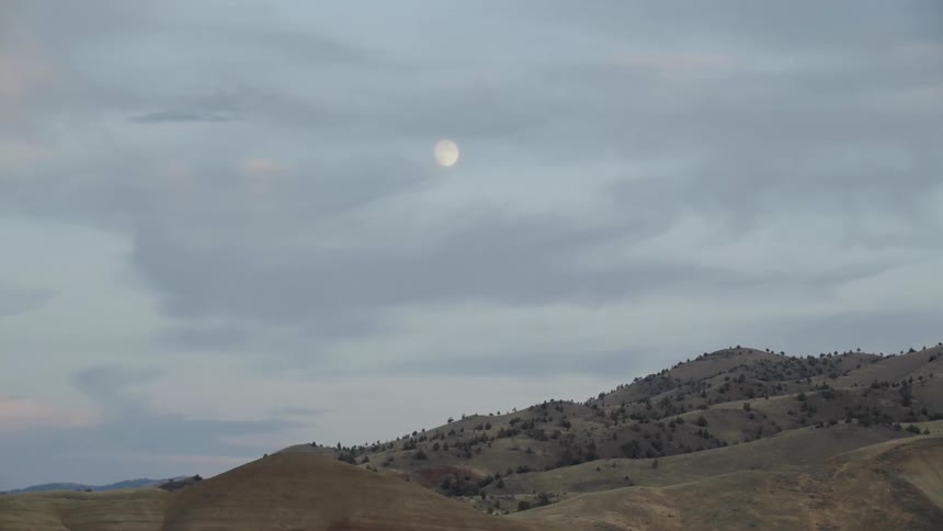 The moon looming over a hill countryside on a cloudy evening