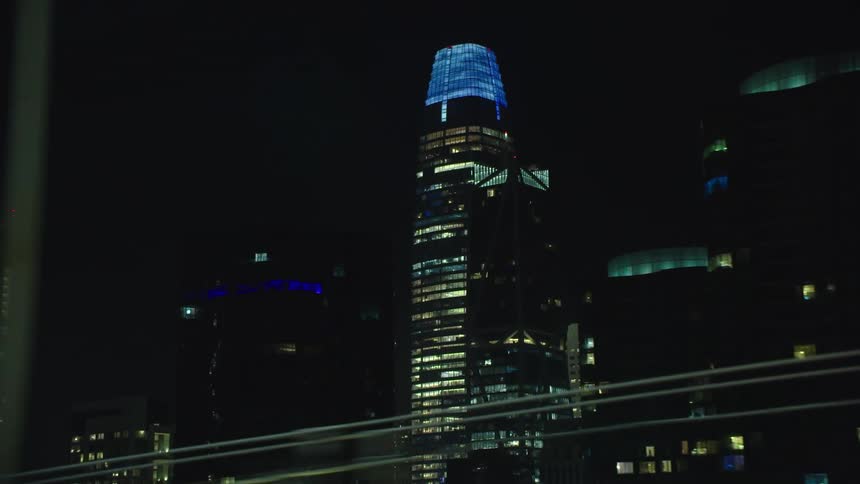 A skyscraper with a glowing top looming above a metropolis at night