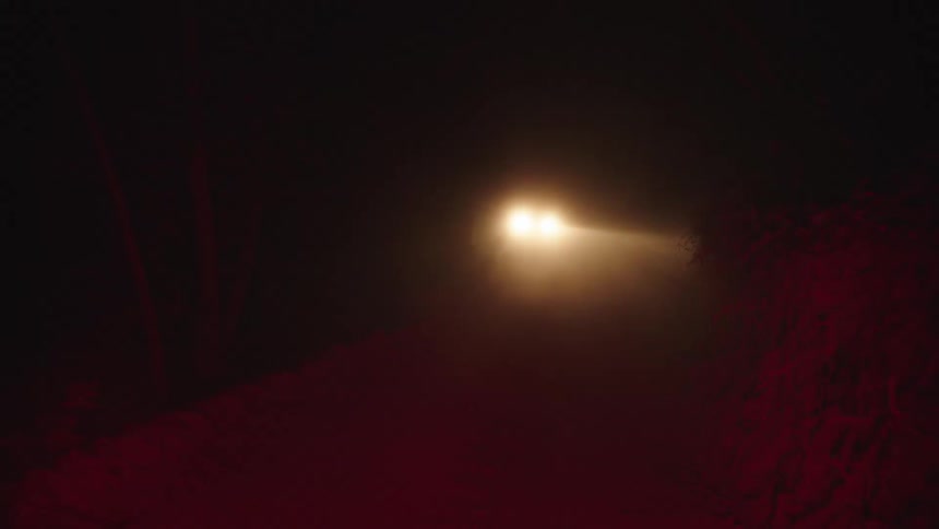A car drives down a dusty road at night