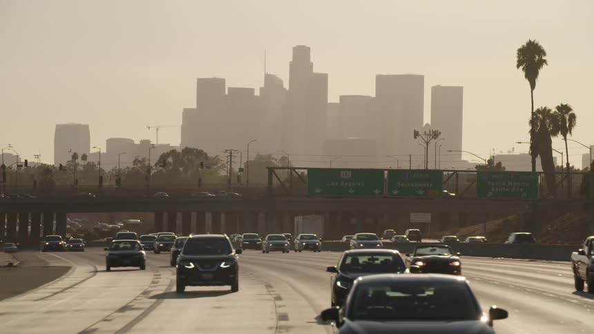 Cars drive along freeway with haze covered city downtown in the background