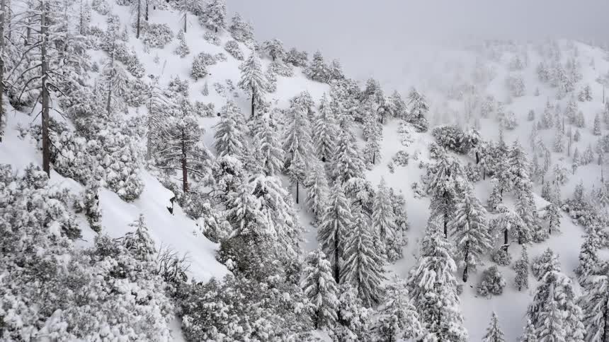 Aerial of fresh snow covered mountain under foggy sky