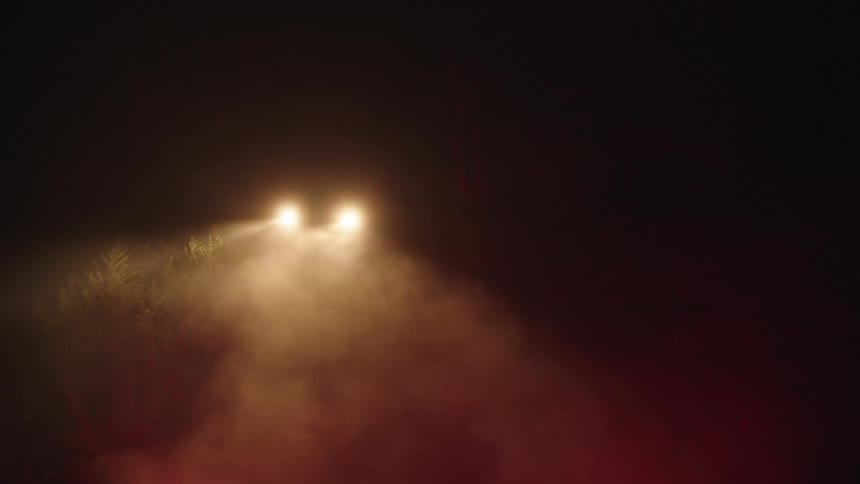 A vehicle driving in the dark with headlights on a dirt road