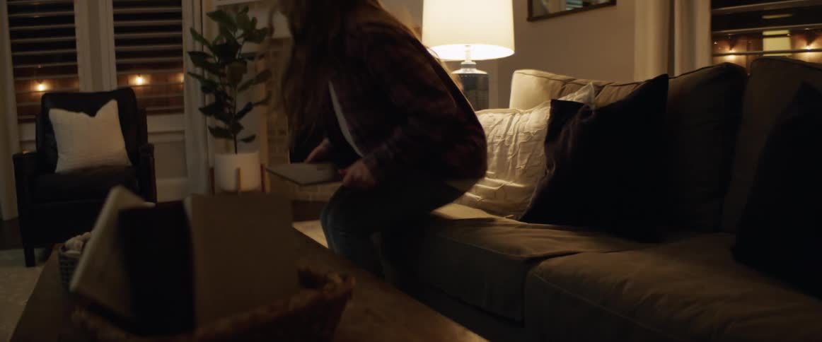 Woman carries a laptop to a sofa then sits down putting her feet on the coffee table