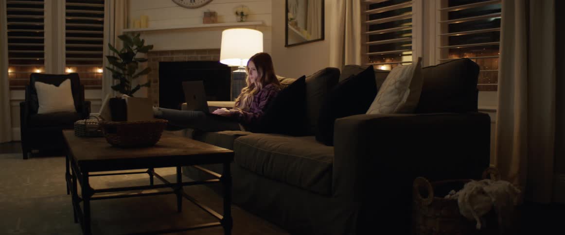 A young girl sits on the couch and uses her laptop