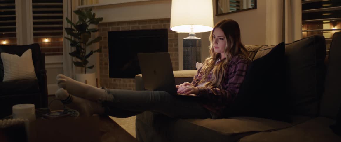 Young woman types on laptop while sitting on sofa in living room