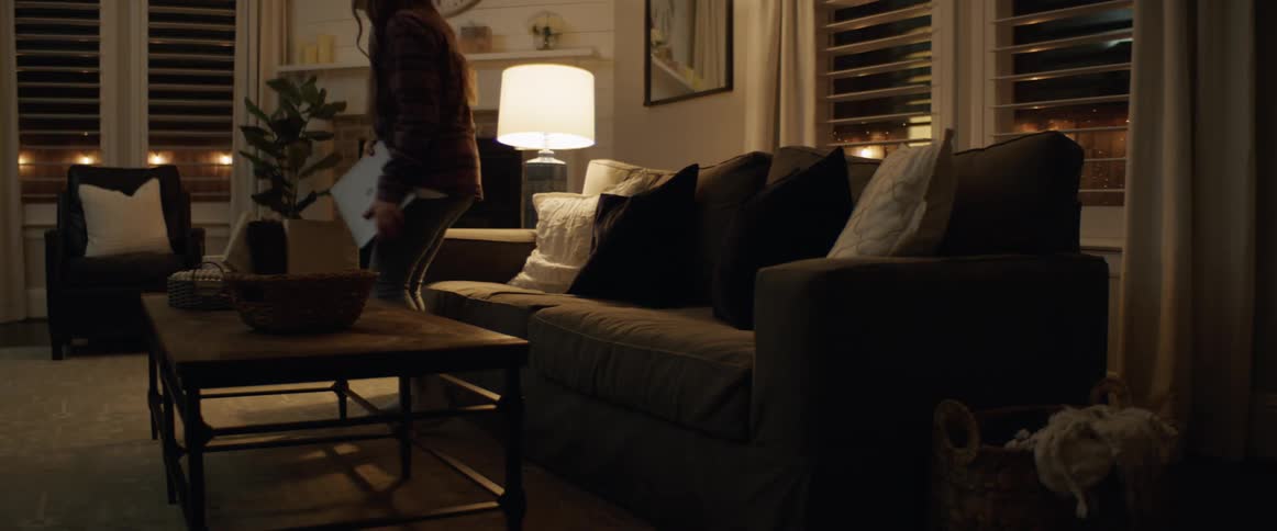 A young woman approaching and sitting on a sofa while carrying a laptop