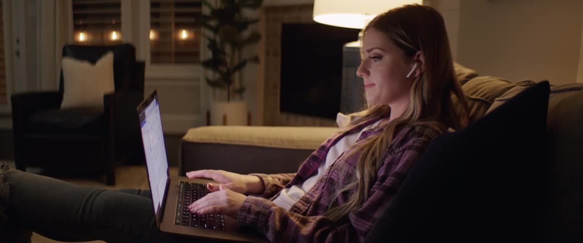 Woman sitting in couch works on a laptop in the living room at night