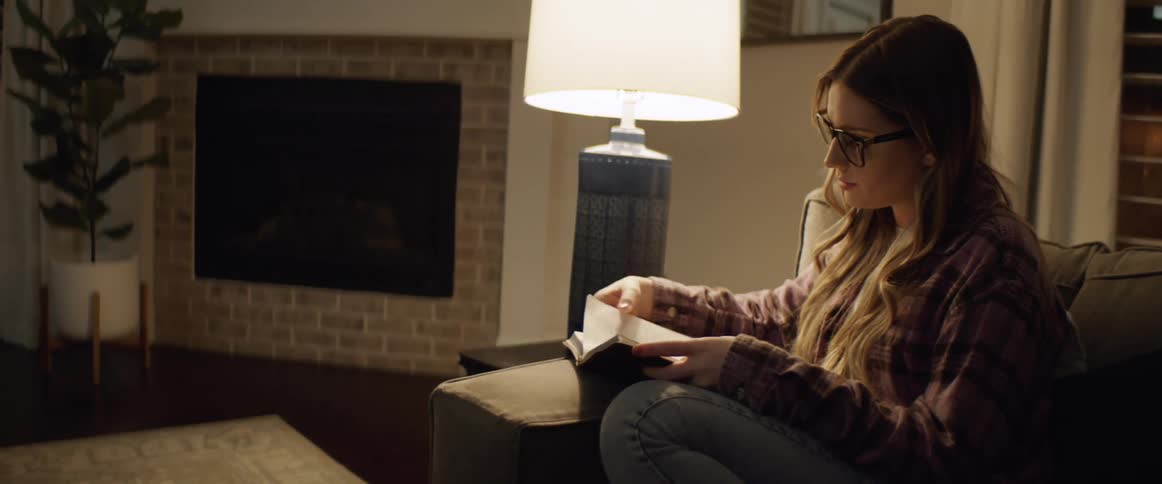 A woman reading a book while sitting in a chair near a lamp