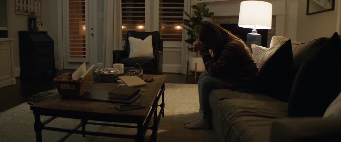 A woman sitting on a sofa in a living room resting her forehead on her fists